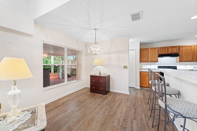 kitchen with light hardwood / wood-style flooring, a notable chandelier, a textured ceiling, and decorative light fixtures