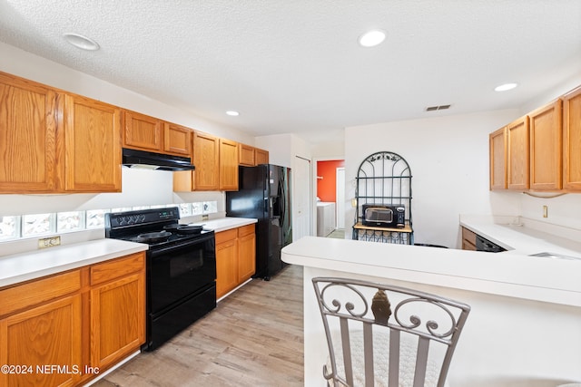 kitchen with black appliances, light wood-type flooring, washing machine and clothes dryer, and a textured ceiling