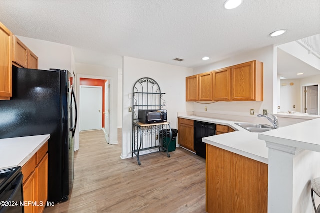 kitchen with kitchen peninsula, black appliances, a textured ceiling, sink, and light hardwood / wood-style flooring