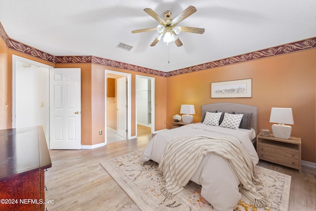 bedroom with light hardwood / wood-style floors, ceiling fan, a spacious closet, and ensuite bathroom