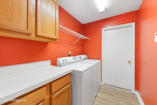 laundry area with a textured ceiling, light wood-type flooring, washer and clothes dryer, and cabinets