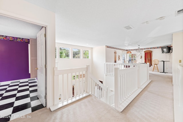 hall with a textured ceiling, light carpet, and an inviting chandelier