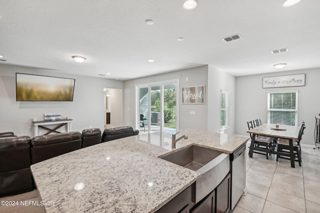 kitchen featuring light stone counters, a center island with sink, light tile patterned floors, sink, and stainless steel dishwasher