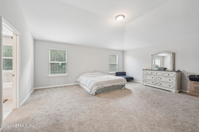 carpeted bedroom with ensuite bath, a textured ceiling, and vaulted ceiling