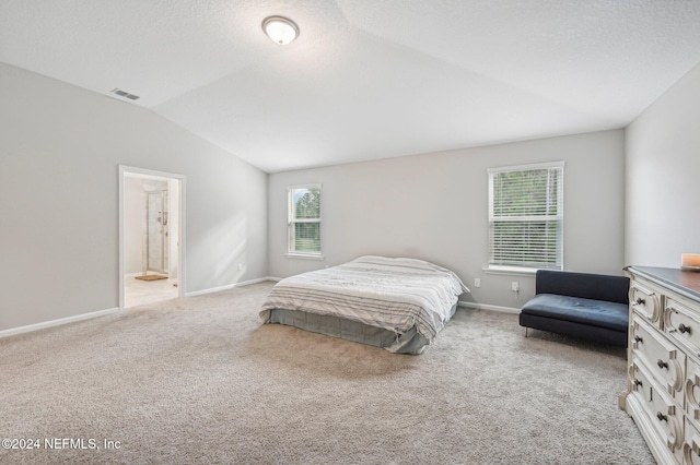 bedroom featuring connected bathroom, light carpet, multiple windows, and lofted ceiling