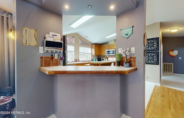 kitchen featuring kitchen peninsula, light hardwood / wood-style floors, and vaulted ceiling