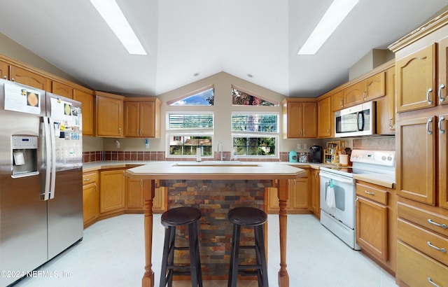 kitchen with a center island with sink, sink, appliances with stainless steel finishes, a kitchen breakfast bar, and vaulted ceiling