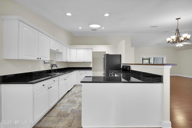 kitchen featuring sink, stainless steel refrigerator, white cabinetry, decorative light fixtures, and kitchen peninsula