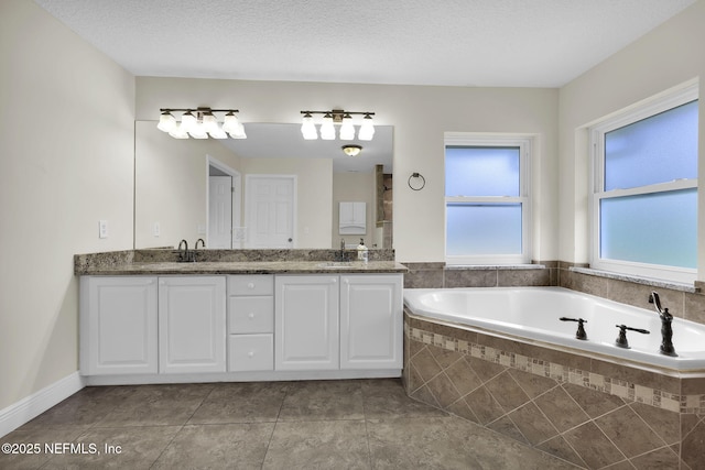 bathroom with vanity, tile patterned flooring, tiled bath, and a textured ceiling