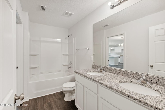 full bathroom with wood-type flooring, vanity,  shower combination, toilet, and a textured ceiling