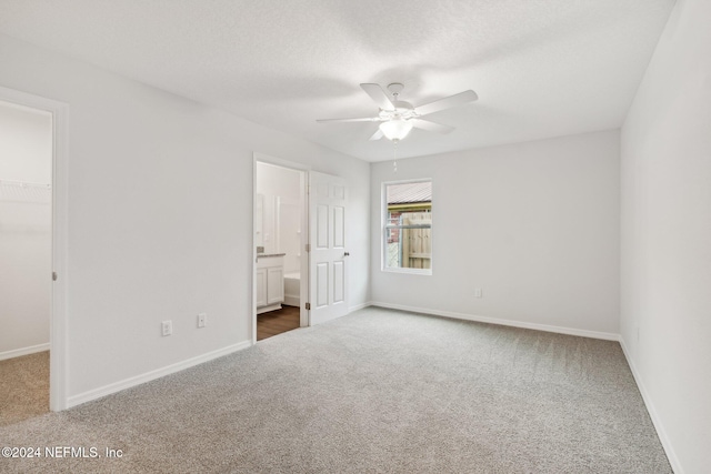 unfurnished bedroom with ensuite bathroom, a textured ceiling, dark carpet, a walk in closet, and a closet