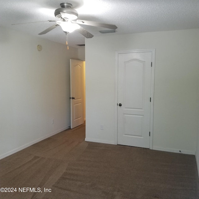 unfurnished bedroom with ceiling fan, dark carpet, and a textured ceiling