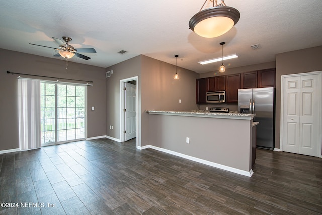 kitchen featuring stainless steel appliances, light stone counters, kitchen peninsula, decorative light fixtures, and dark wood-type flooring