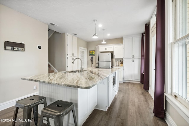 kitchen featuring white cabinetry, sink, light stone counters, dark hardwood / wood-style floors, and white refrigerator