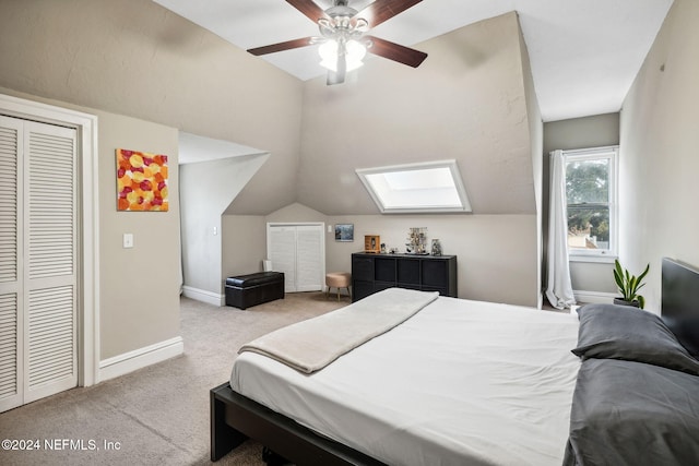 bedroom featuring a closet, vaulted ceiling with skylight, light colored carpet, and ceiling fan