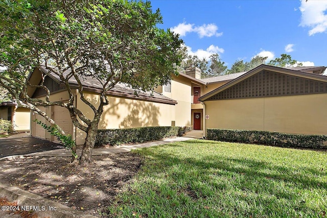 exterior space with a garage, a lawn, a chimney, and stucco siding