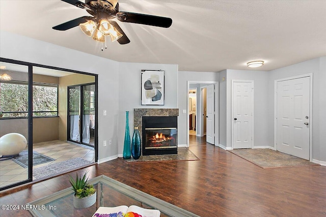 living room with wood finished floors, a tile fireplace, a ceiling fan, and baseboards