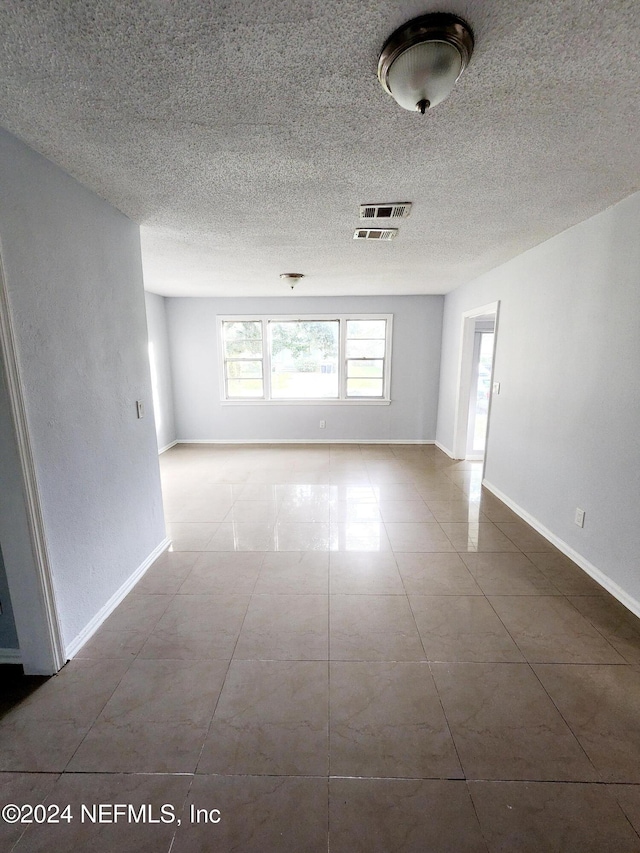 tiled empty room featuring a textured ceiling