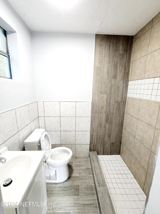 bathroom featuring vanity, a textured ceiling, toilet, and tile walls