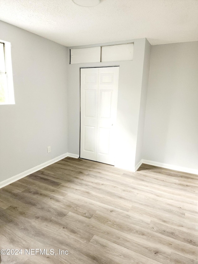 unfurnished bedroom featuring a closet, a textured ceiling, and light hardwood / wood-style flooring