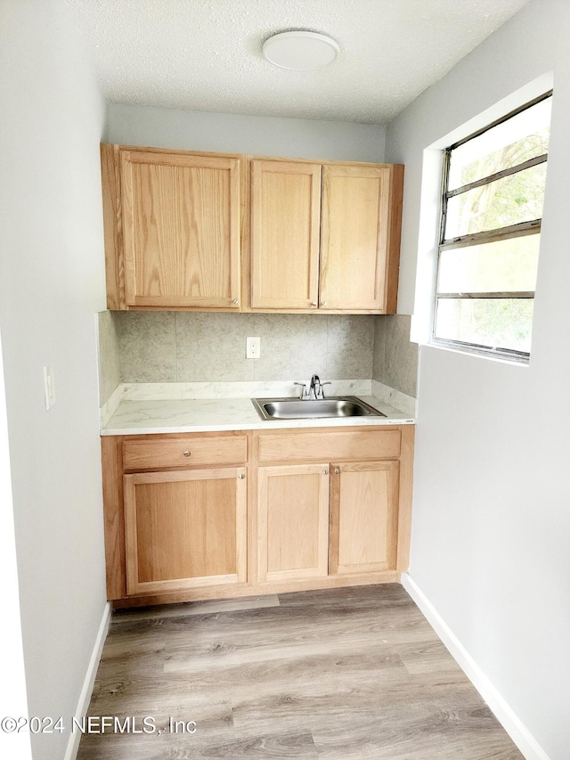 kitchen with light brown cabinetry, tasteful backsplash, a textured ceiling, sink, and light hardwood / wood-style flooring