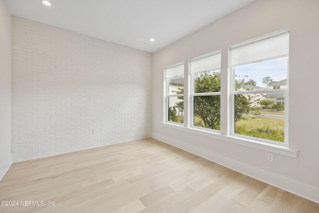 empty room with brick wall and light hardwood / wood-style flooring