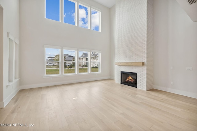 unfurnished living room featuring a towering ceiling, light hardwood / wood-style floors, a brick fireplace, and a healthy amount of sunlight