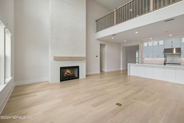 unfurnished living room with a towering ceiling, a large fireplace, and light hardwood / wood-style flooring