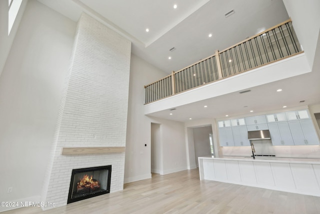 unfurnished living room with a towering ceiling, a large fireplace, and light hardwood / wood-style flooring