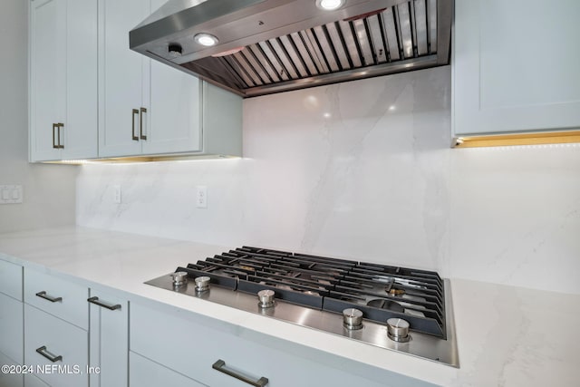 kitchen with light stone countertops, decorative backsplash, exhaust hood, and stainless steel gas cooktop