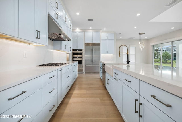 kitchen with white cabinetry, sink, hanging light fixtures, stainless steel appliances, and light hardwood / wood-style floors