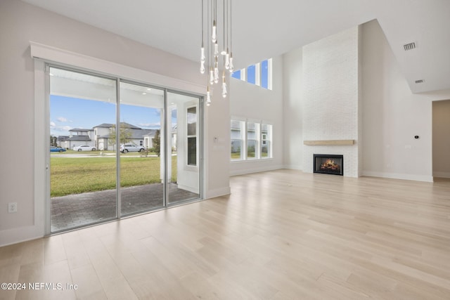 unfurnished living room featuring a fireplace, a high ceiling, and light wood-type flooring