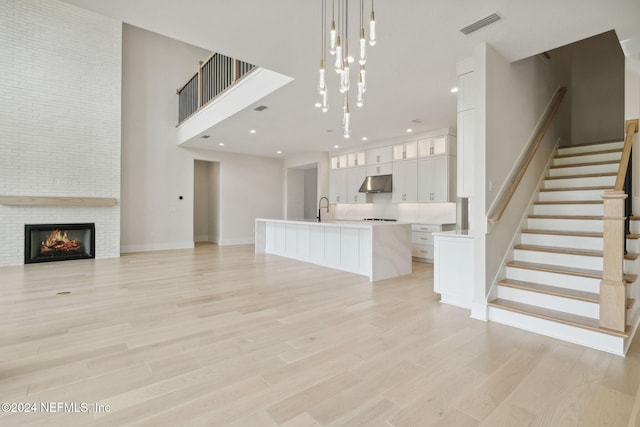 unfurnished living room with a large fireplace, sink, a towering ceiling, and light wood-type flooring