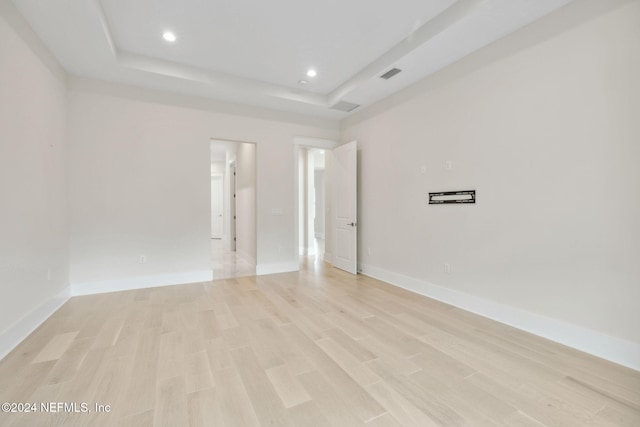 spare room with a raised ceiling and light wood-type flooring