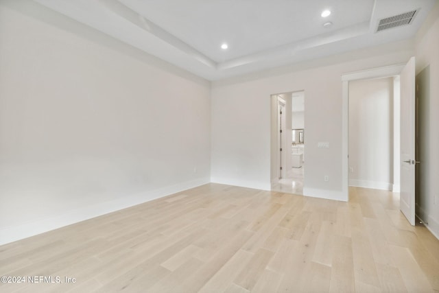 spare room with light wood-type flooring and a tray ceiling