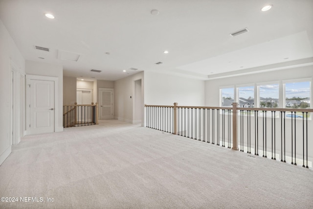 empty room featuring a raised ceiling and light colored carpet