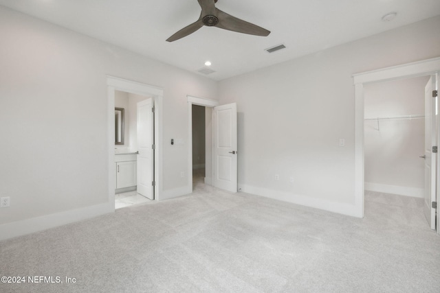 unfurnished bedroom featuring a walk in closet, ensuite bathroom, light colored carpet, ceiling fan, and a closet