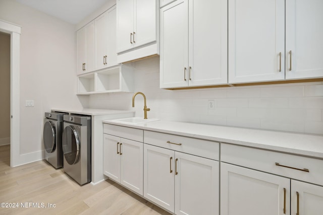 washroom featuring washing machine and dryer, cabinets, sink, and light hardwood / wood-style floors