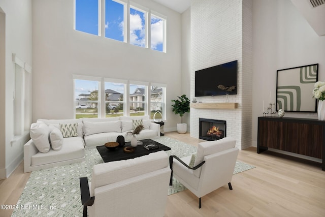 living room with a towering ceiling, a fireplace, and light hardwood / wood-style flooring