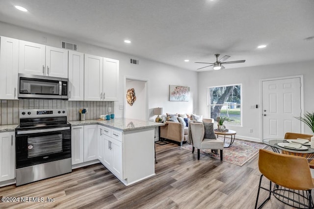 kitchen with white cabinets, kitchen peninsula, stainless steel appliances, and light hardwood / wood-style flooring