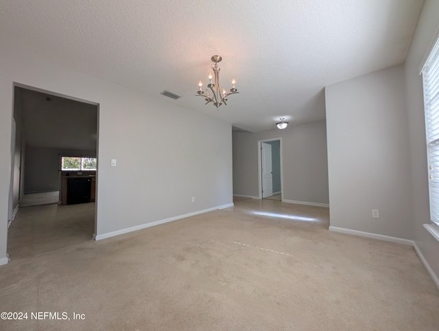 carpeted spare room featuring a textured ceiling and a chandelier