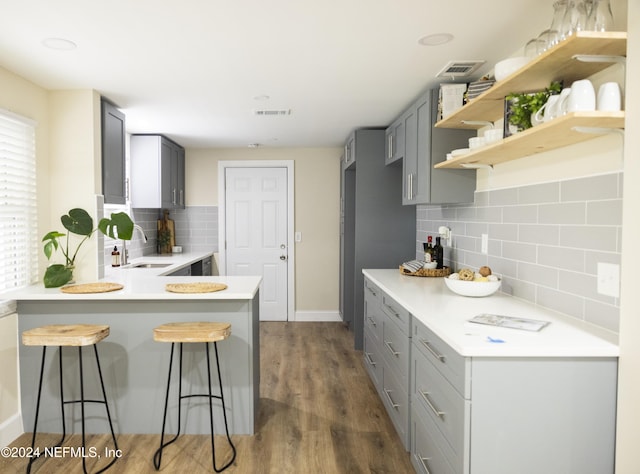 kitchen featuring sink, decorative backsplash, kitchen peninsula, gray cabinetry, and dark hardwood / wood-style flooring