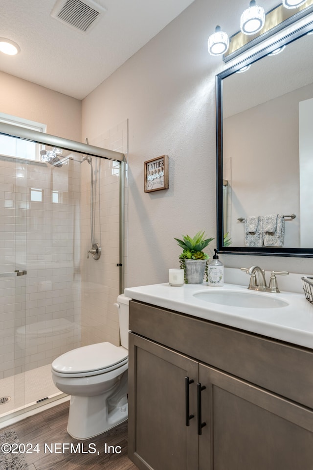 bathroom featuring toilet, vanity, hardwood / wood-style flooring, and a shower with door