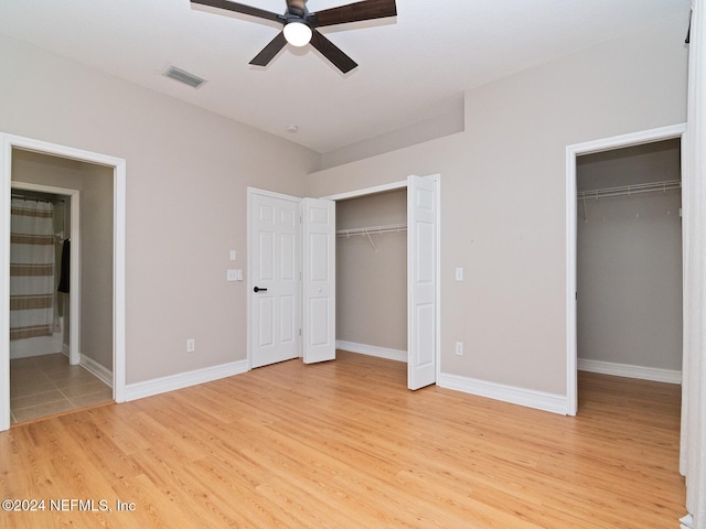 unfurnished bedroom with ensuite bathroom, light hardwood / wood-style flooring, ceiling fan, and two closets