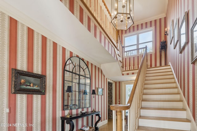 stairway with hardwood / wood-style flooring, a towering ceiling, a chandelier, and ornamental molding