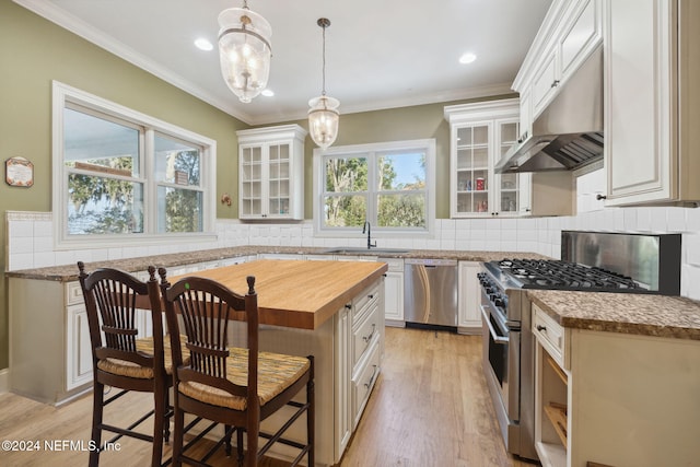 kitchen with stainless steel appliances, a center island, hanging light fixtures, white cabinetry, and range hood