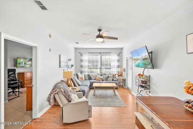 living room featuring ceiling fan, light hardwood / wood-style floors, and a textured ceiling