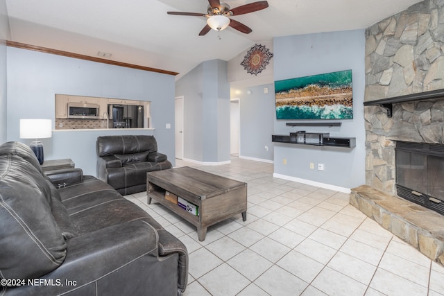 tiled living room with ceiling fan, a stone fireplace, and vaulted ceiling