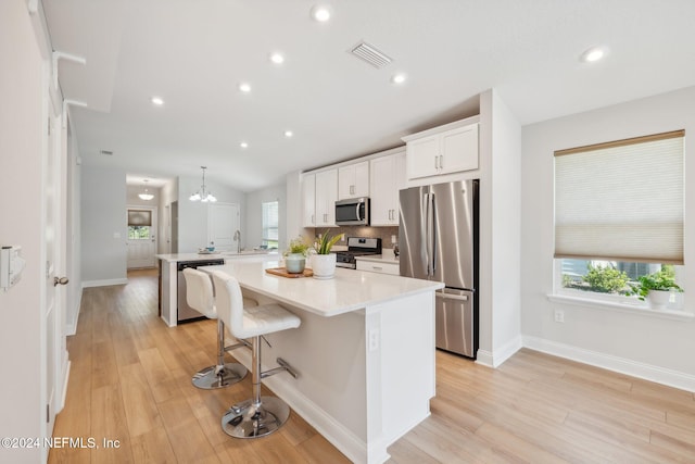 kitchen featuring white cabinetry, a center island, stainless steel appliances, a kitchen breakfast bar, and decorative light fixtures