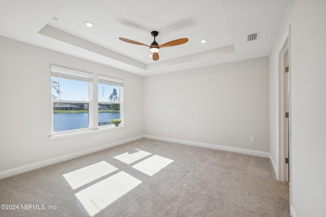 carpeted empty room with ceiling fan, a water view, and a tray ceiling